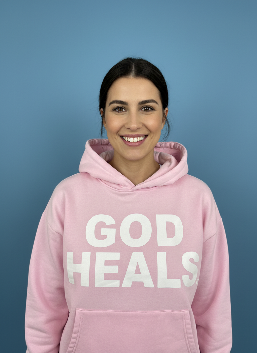 Hoodie ‘God Heals’ voor dames, christelijke streetwear-mode tegen een blauwe achtergrond.