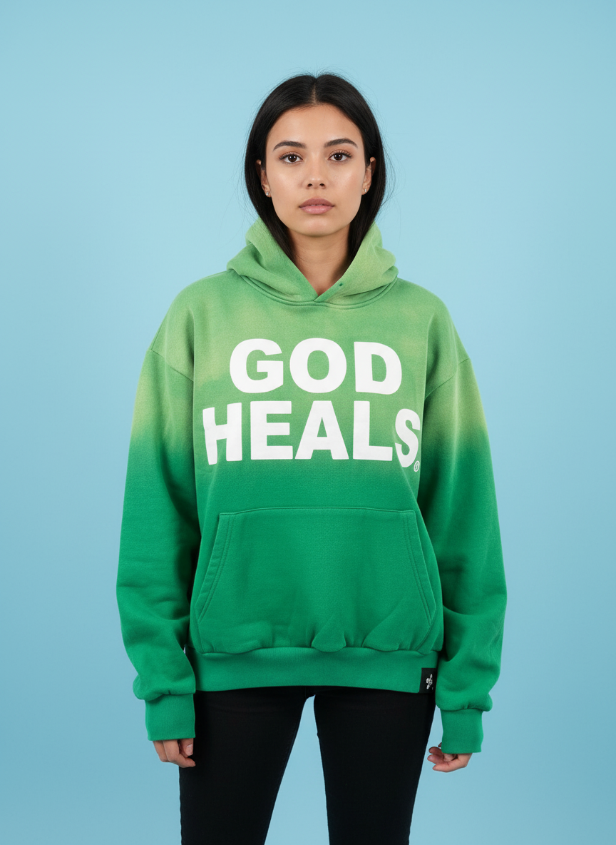 Hoodie ‘God Heals’ voor dames, christelijke streetwear-mode tegen een blauwe achtergrond.