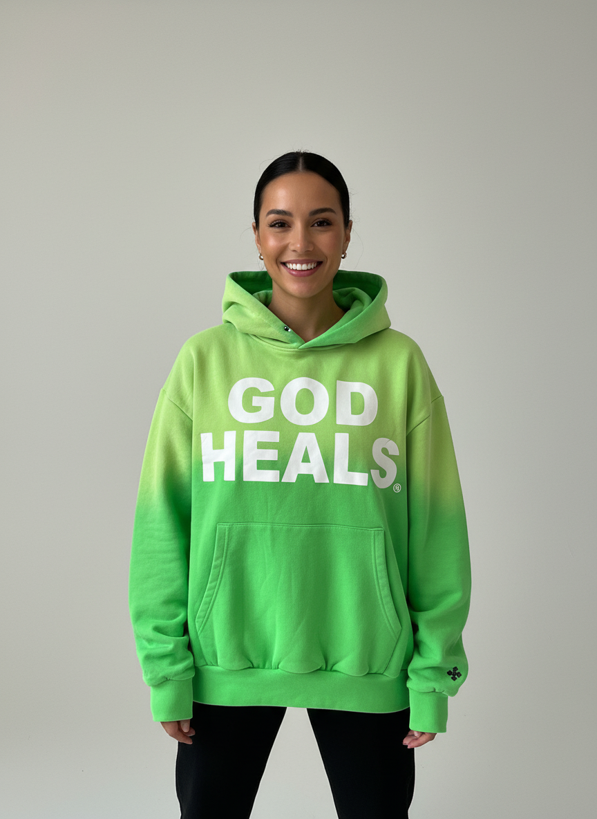 Hoodie ‘God Heals’ voor dames, christelijke streetwear-mode tegen een lichtgrijze achtergrond.