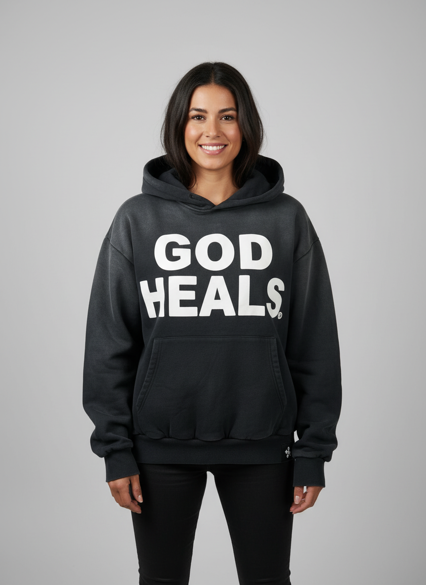 Hoodie ‘God Heals’ voor dames, christelijke streetwear-mode tegen een lichtgrijze achtergrond.